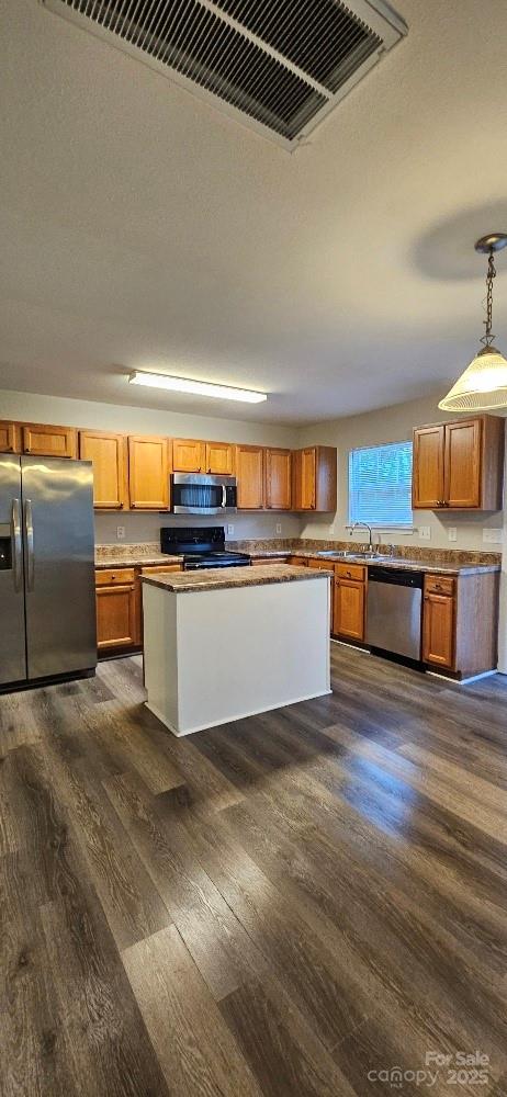 kitchen with appliances with stainless steel finishes, dark wood-type flooring, brown cabinetry, a sink, and hanging light fixtures