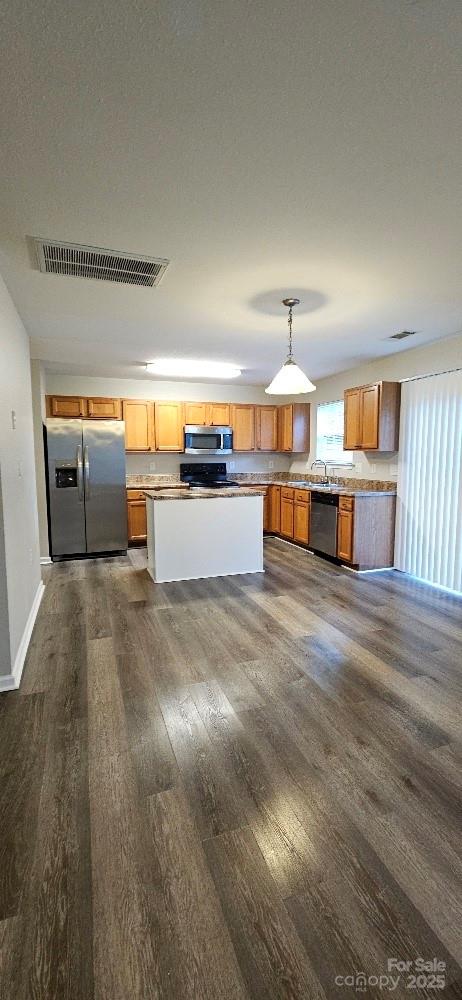kitchen with stainless steel appliances, dark wood-type flooring, pendant lighting, light countertops, and a kitchen island
