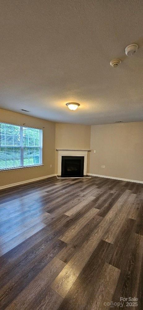 unfurnished living room with dark wood-type flooring, a fireplace, baseboards, and a textured ceiling