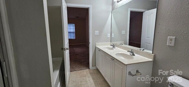 full bath featuring toilet, double vanity, a textured wall, tile patterned floors, and a bath
