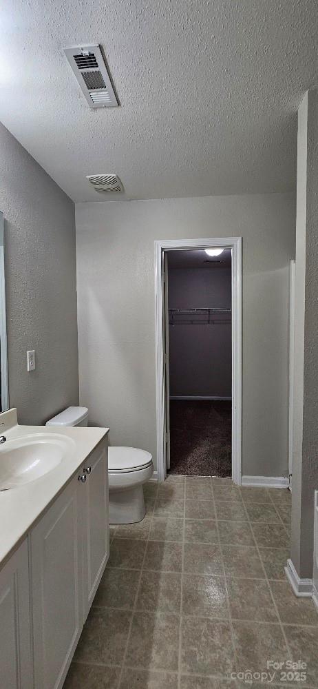bathroom featuring vanity, toilet, a textured ceiling, and a spacious closet