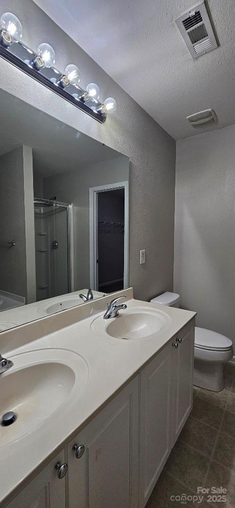 full bathroom featuring a shower stall, double vanity, a textured ceiling, and toilet
