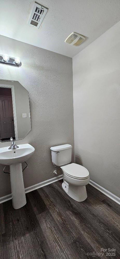 half bath featuring wood finished floors, toilet, and baseboards