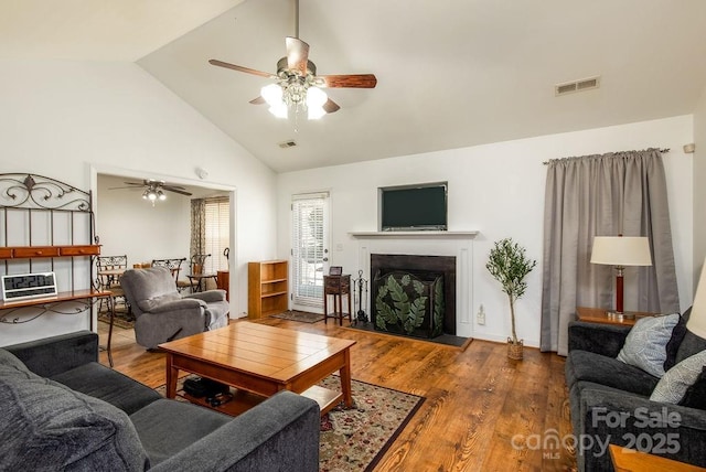 living area featuring a fireplace with raised hearth, vaulted ceiling, visible vents, and wood finished floors