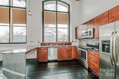 kitchen featuring dark wood-style floors, a sink, decorative backsplash, appliances with stainless steel finishes, and brown cabinets