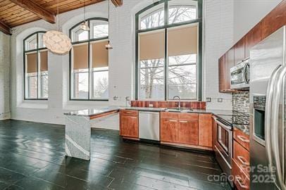 kitchen with beamed ceiling, brown cabinets, plenty of natural light, stainless steel appliances, and wood ceiling