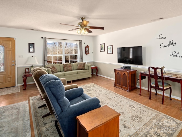 living area featuring a textured ceiling, wood finished floors, visible vents, and a ceiling fan