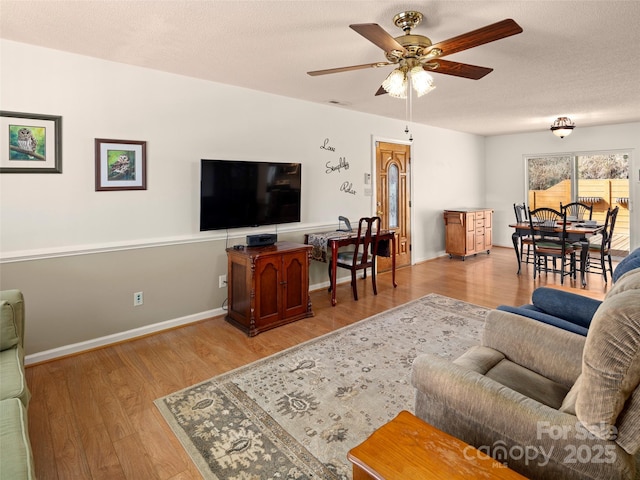 living area with light wood-style floors, a textured ceiling, baseboards, and a ceiling fan