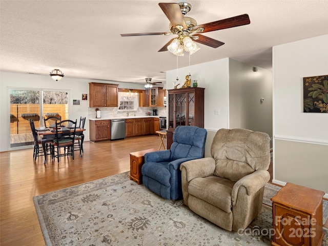 living room featuring light wood-type flooring, a ceiling fan, and a textured ceiling