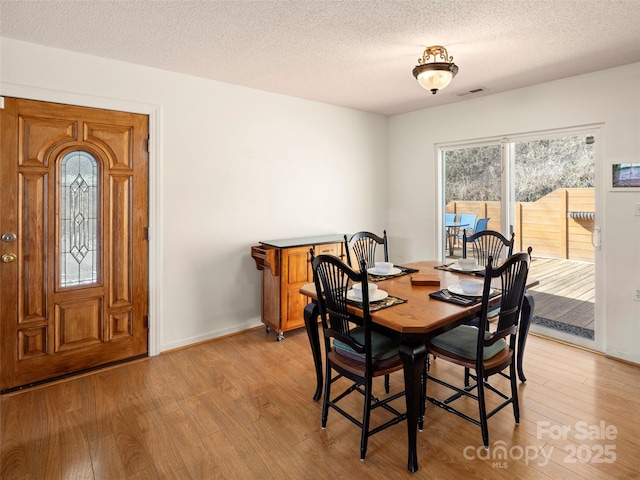 dining area featuring light wood-style floors, a wealth of natural light, a textured ceiling, and baseboards