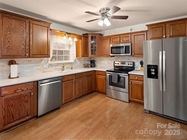 kitchen featuring light wood finished floors, brown cabinetry, stainless steel appliances, light countertops, and a sink