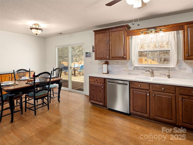 kitchen with a sink, light wood-style floors, light countertops, stainless steel dishwasher, and decorative backsplash