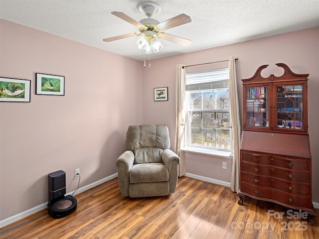 sitting room with a textured ceiling, wood finished floors, a ceiling fan, and baseboards