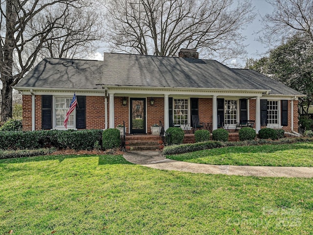 view of front of home featuring brick siding, a chimney, a shingled roof, covered porch, and a front yard