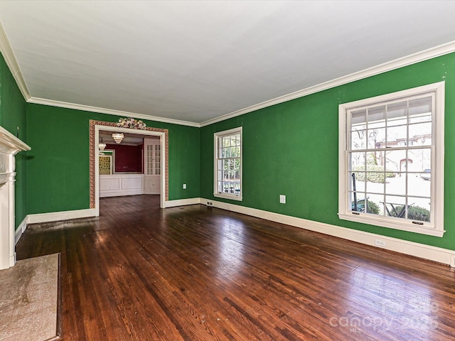 empty room with crown molding, a fireplace, baseboards, and wood finished floors