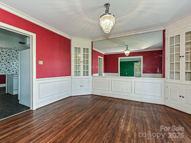 unfurnished dining area featuring a chandelier, a wainscoted wall, crown molding, and wood finished floors