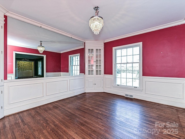 empty room with wainscoting, visible vents, a notable chandelier, and wood finished floors