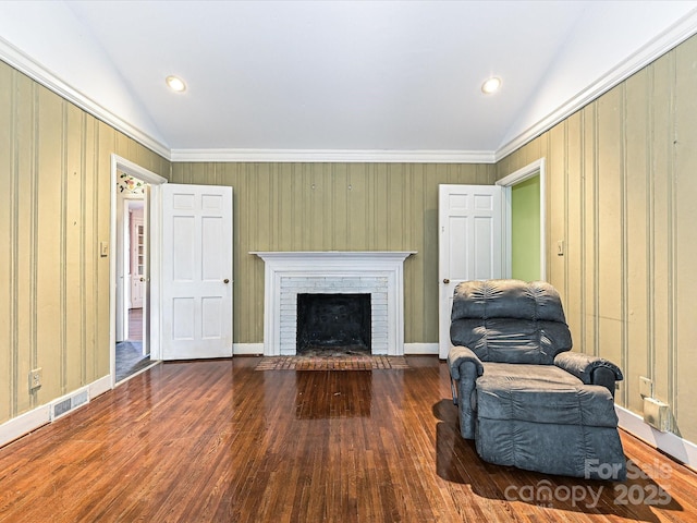 living area with lofted ceiling, a brick fireplace, visible vents, and wood finished floors