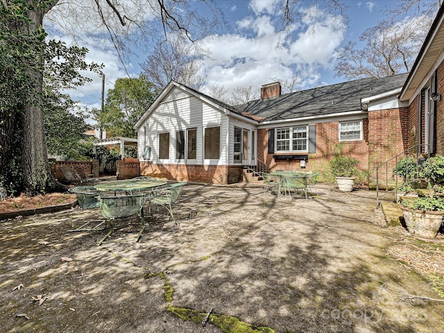 back of house with entry steps, brick siding, a chimney, and a patio area