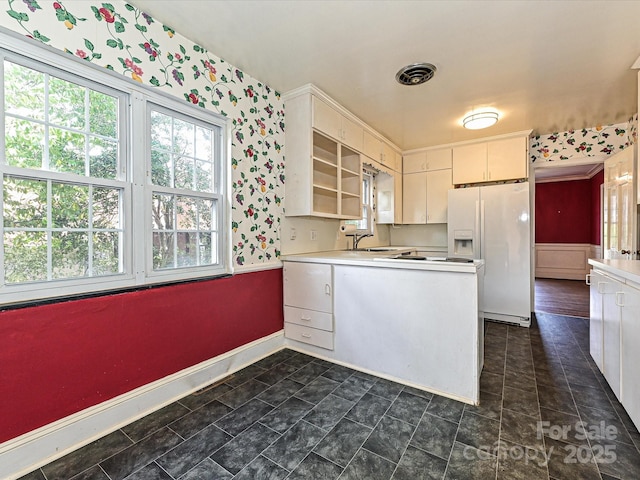 kitchen featuring a peninsula, visible vents, light countertops, white fridge with ice dispenser, and wallpapered walls