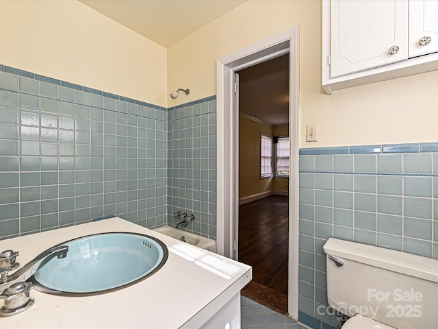 full bath with tile walls, toilet, wainscoting, a sink, and  shower combination