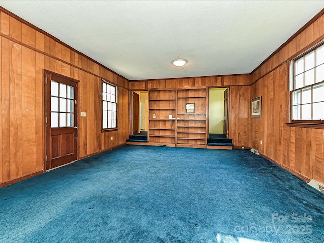 spare room with wood walls, visible vents, dark carpet, and crown molding