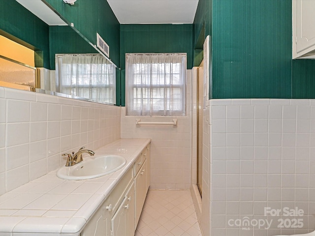 bathroom with visible vents, vanity, tile walls, tile patterned floors, and a stall shower