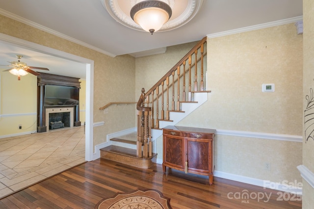 staircase with crown molding, a fireplace, ceiling fan, baseboards, and hardwood / wood-style flooring