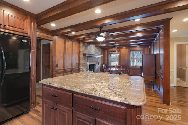 kitchen featuring light stone counters, a fireplace, light wood-style floors, freestanding refrigerator, and beamed ceiling