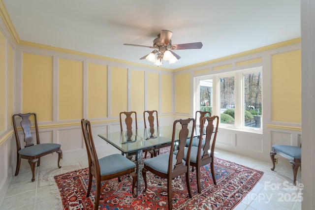 dining room featuring ornamental molding, light tile patterned floors, a decorative wall, and a ceiling fan