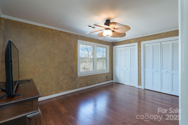 unfurnished bedroom with wood finished floors, visible vents, baseboards, multiple closets, and ornamental molding