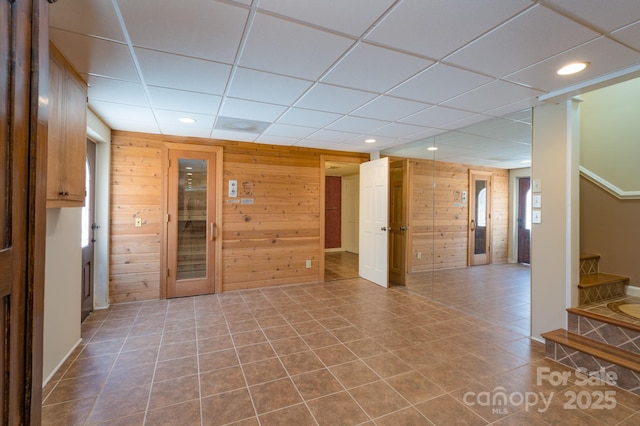 empty room with dark tile patterned floors, wood walls, stairway, and recessed lighting