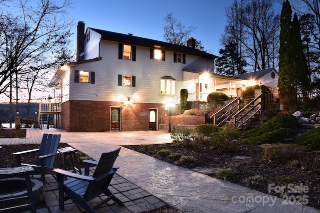 rear view of house featuring brick siding, a chimney, a patio area, and stairway