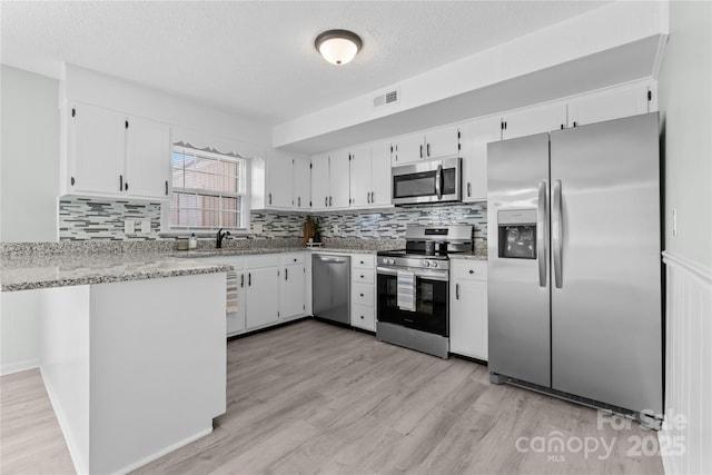 kitchen featuring stainless steel appliances, visible vents, light wood-style flooring, decorative backsplash, and white cabinets