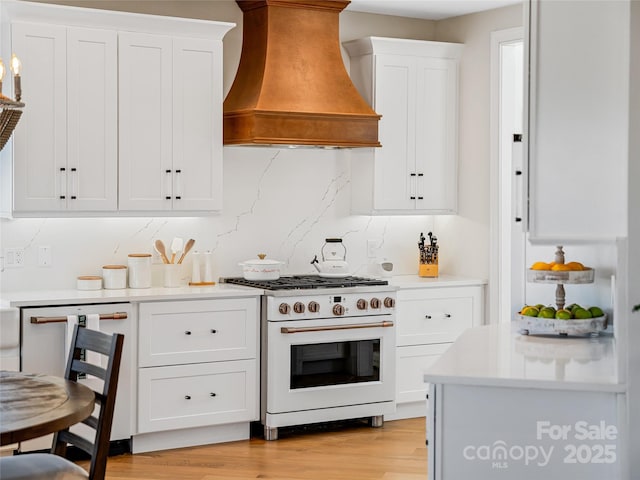 kitchen with light wood-style flooring, light countertops, custom range hood, white gas range oven, and white cabinetry