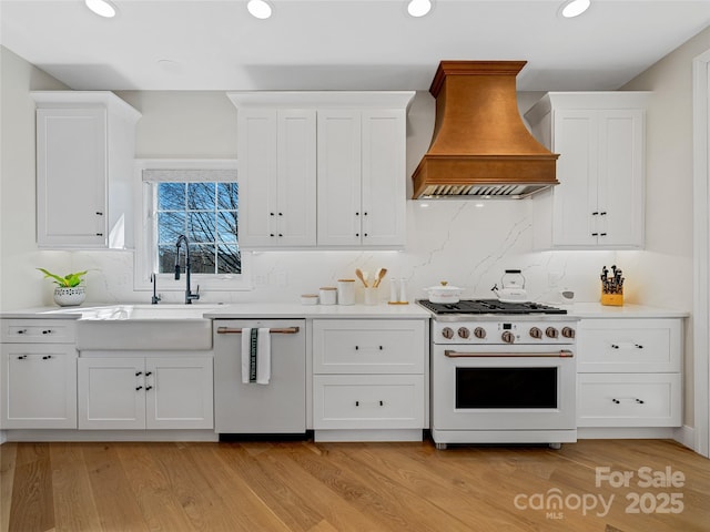 kitchen with high end stove, white cabinetry, light countertops, dishwashing machine, and custom exhaust hood