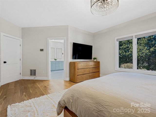 bedroom featuring wood finished floors, visible vents, baseboards, ensuite bathroom, and a notable chandelier