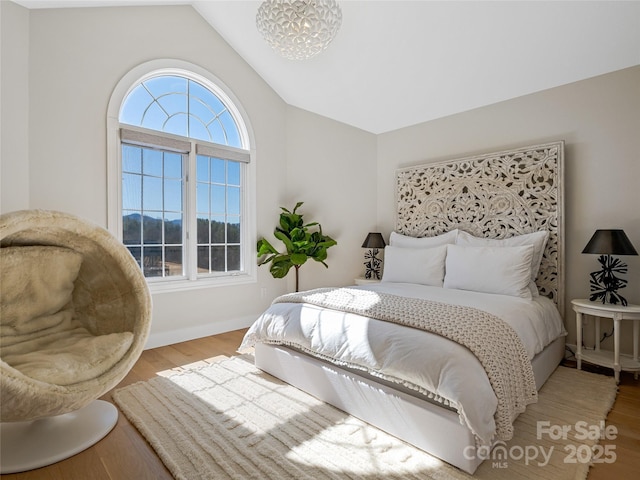 bedroom featuring vaulted ceiling, a notable chandelier, wood finished floors, and baseboards