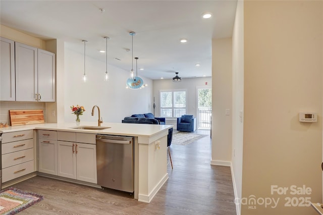 kitchen with light countertops, open floor plan, a sink, dishwasher, and a peninsula