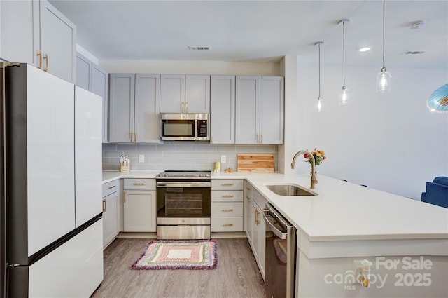 kitchen featuring appliances with stainless steel finishes, light countertops, a sink, and a peninsula