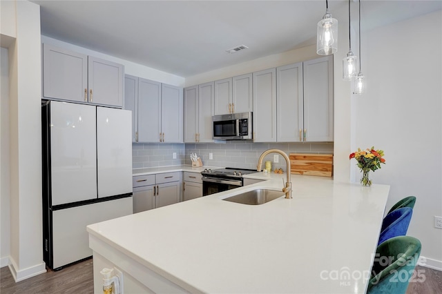 kitchen with visible vents, a peninsula, a sink, stainless steel appliances, and backsplash