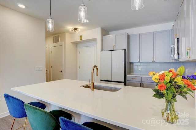 kitchen featuring pendant lighting, tasteful backsplash, visible vents, freestanding refrigerator, and a sink