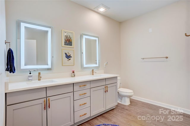 bathroom with toilet, double vanity, a sink, and wood finished floors