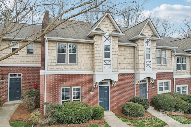 townhome / multi-family property with brick siding, a chimney, and a shingled roof