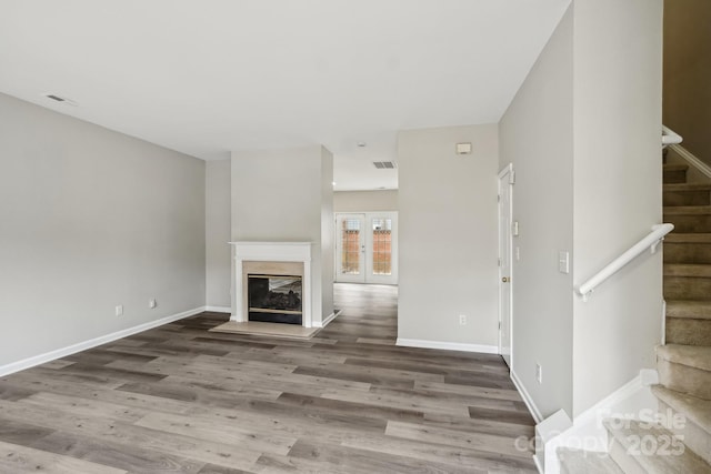 unfurnished living room with visible vents, stairway, a glass covered fireplace, wood finished floors, and baseboards