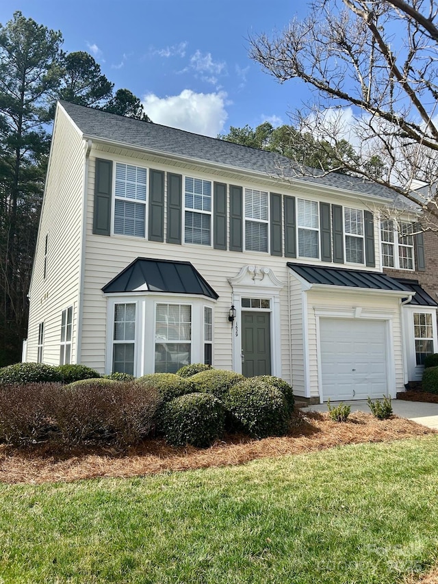 colonial home with metal roof, an attached garage, concrete driveway, a front lawn, and a standing seam roof