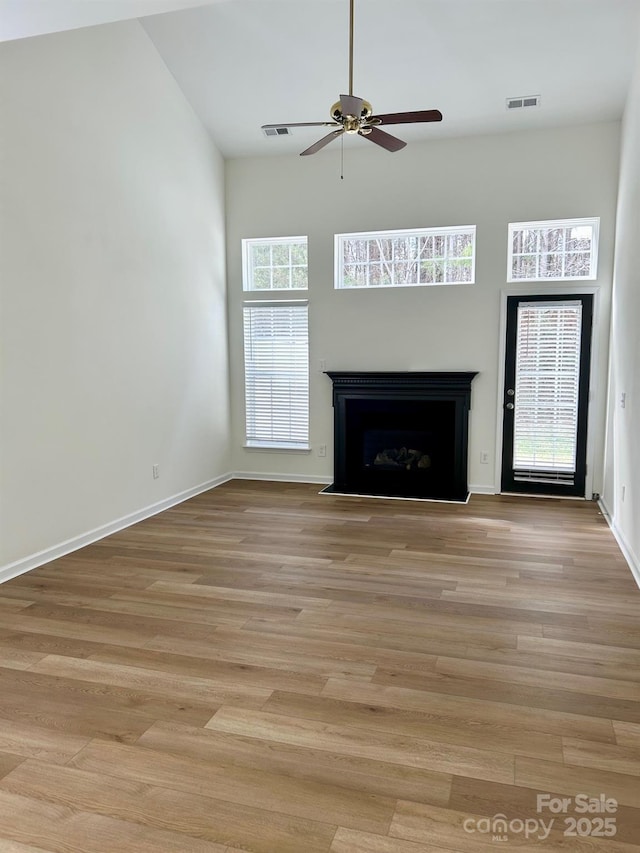 unfurnished living room featuring light wood-type flooring, a fireplace with flush hearth, visible vents, and baseboards