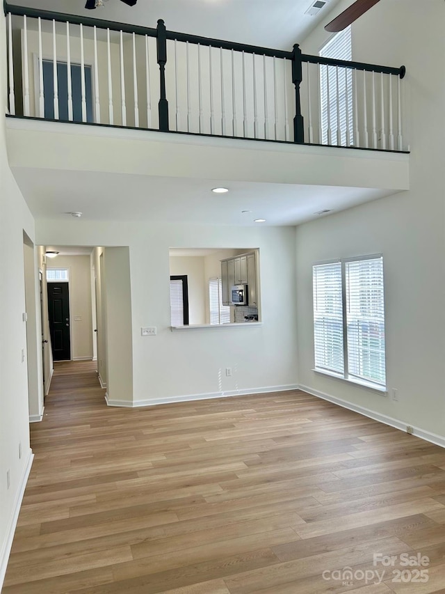 unfurnished living room featuring a ceiling fan, light wood-style floors, a towering ceiling, and baseboards