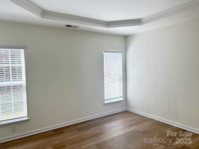 unfurnished room with baseboards, visible vents, ornamental molding, wood finished floors, and a tray ceiling