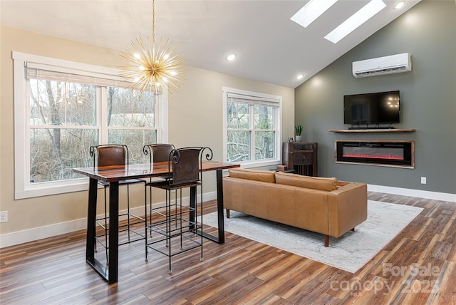 living area featuring a wall unit AC, wood finished floors, baseboards, a glass covered fireplace, and a chandelier